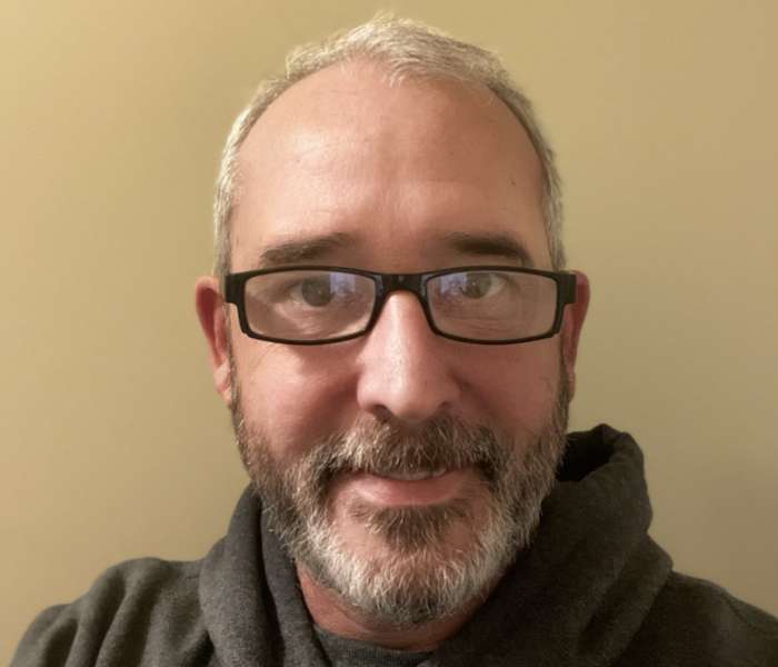 portrait of Craig Stillman in glasses and hoodie smiling at the camera